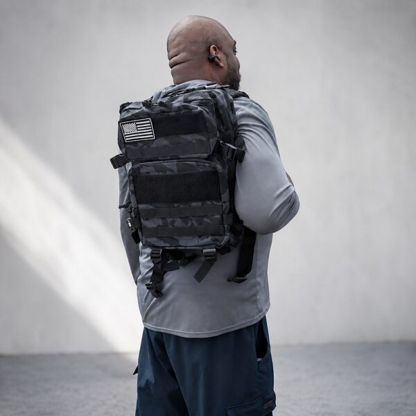 Black camo tactical backpack with MOLLE-style webbing and American flag patch worn by male model